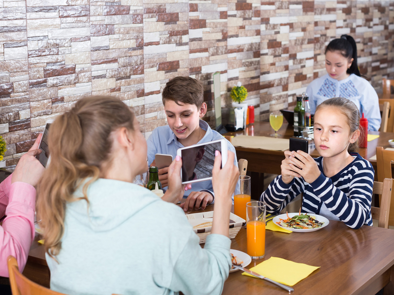 Obitelj sjedi u restoranu i svi gledaju u svoj mobitel